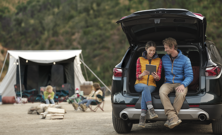 couple sitting in trunk looking at phone at campsite